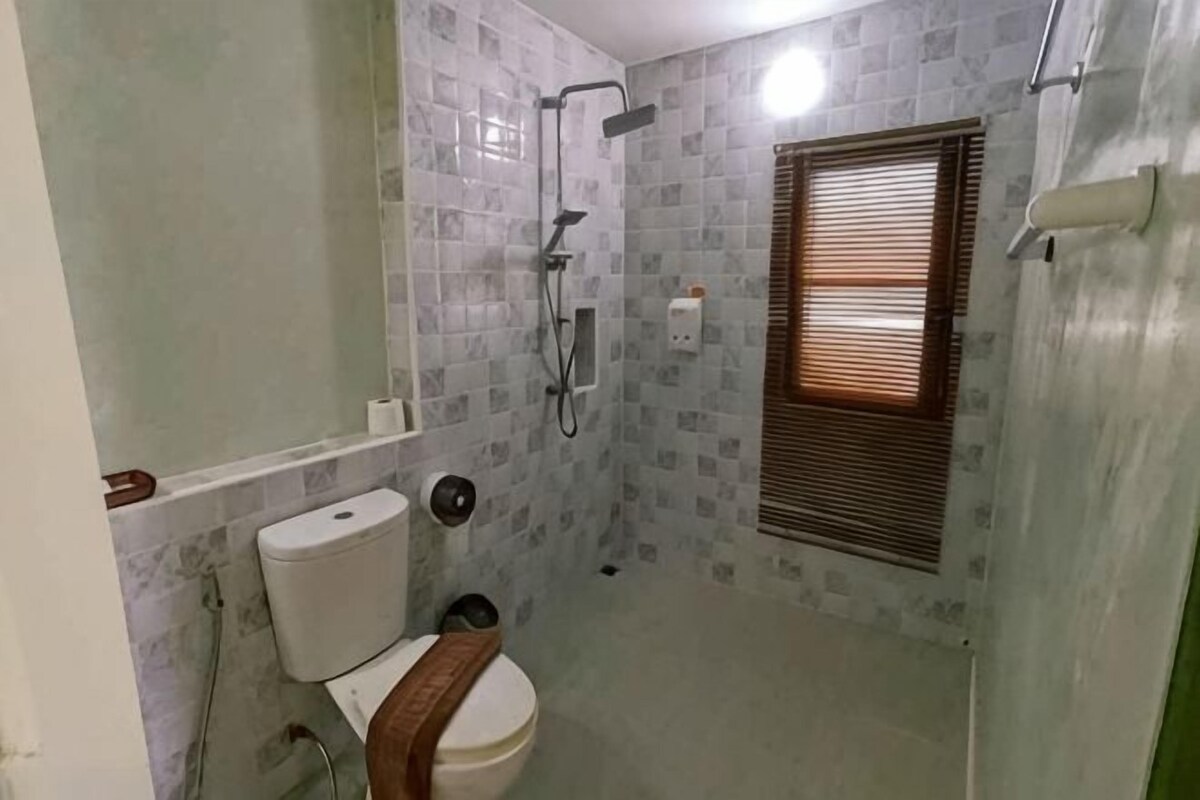 A small bathroom with a toilet, a shower, and a window with blinds.