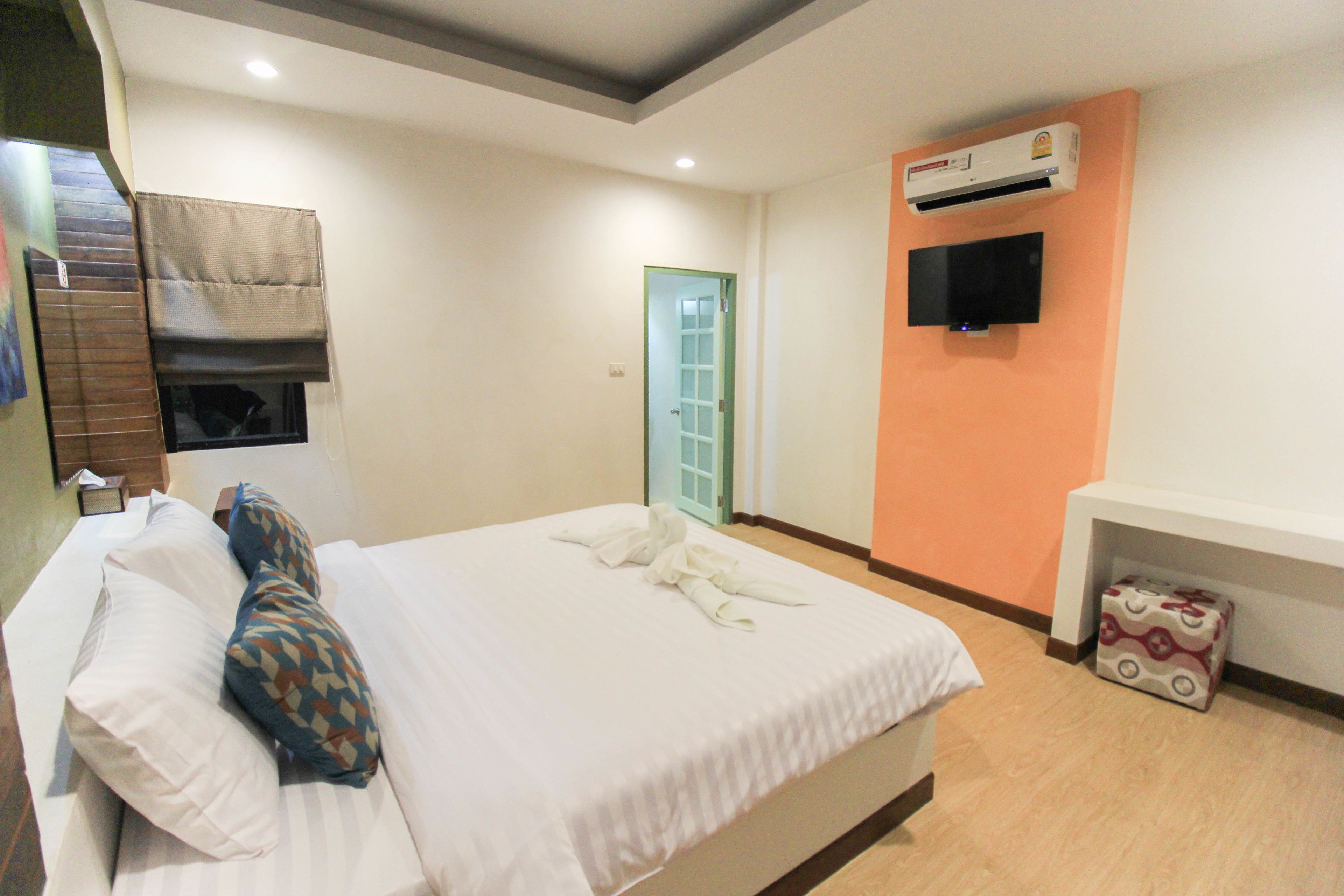 A hotel room with a bed, pillows, a TV, an air conditioner, and a door.