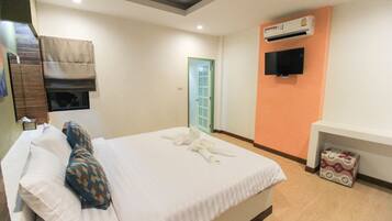 A hotel room with a bed, pillows, a TV, an air conditioner, and a door.