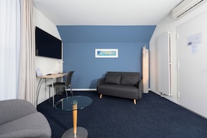 Una habitación moderna con una pared azul de acento, un sofá gris, una mesa de vidrio, un televisor y un radiador.