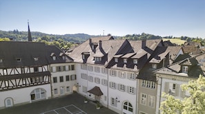 A traditional European building with a prominent tower, a courtyard with a small building, and a view of a forested hill. - Hotel Zofingen (Zofingen)
