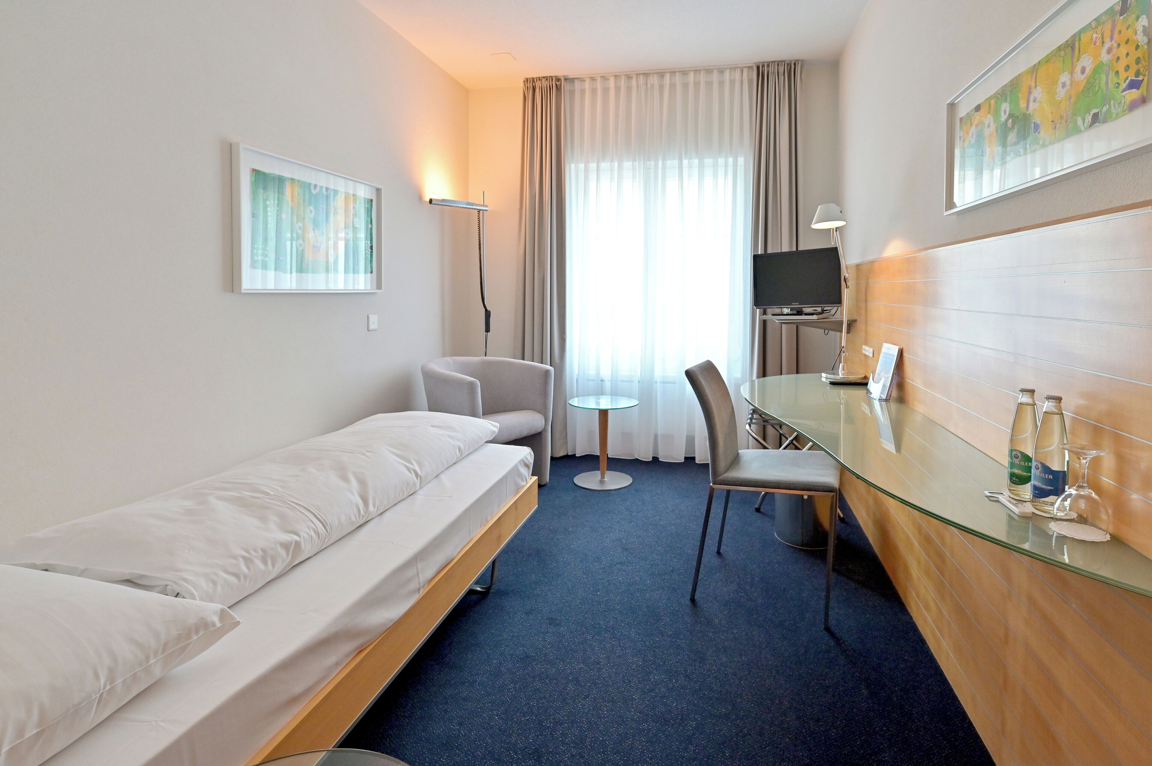 Ein Hotelzimmer mit Bett, Schreibtisch mit Stuhl, Fernseher und einem Bild an der Wand.