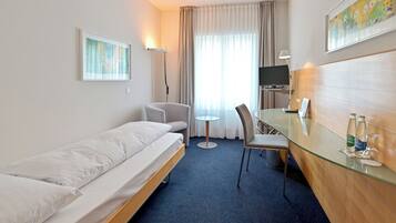 Quarto de hotel com cama, escrivaninha com cadeira, televisão e um quadro na parede.