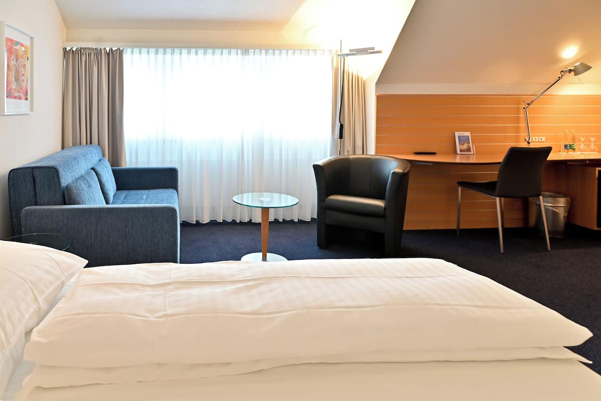 Una habitación de hotel con cama, escritorio, silla, sofá y una mesita.