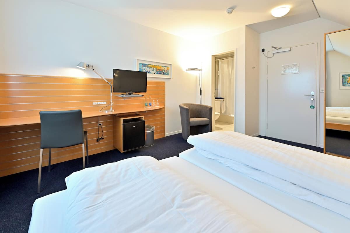 Habitación de hotel con cama, escritorio, silla, televisor y un refrigerador pequeño.