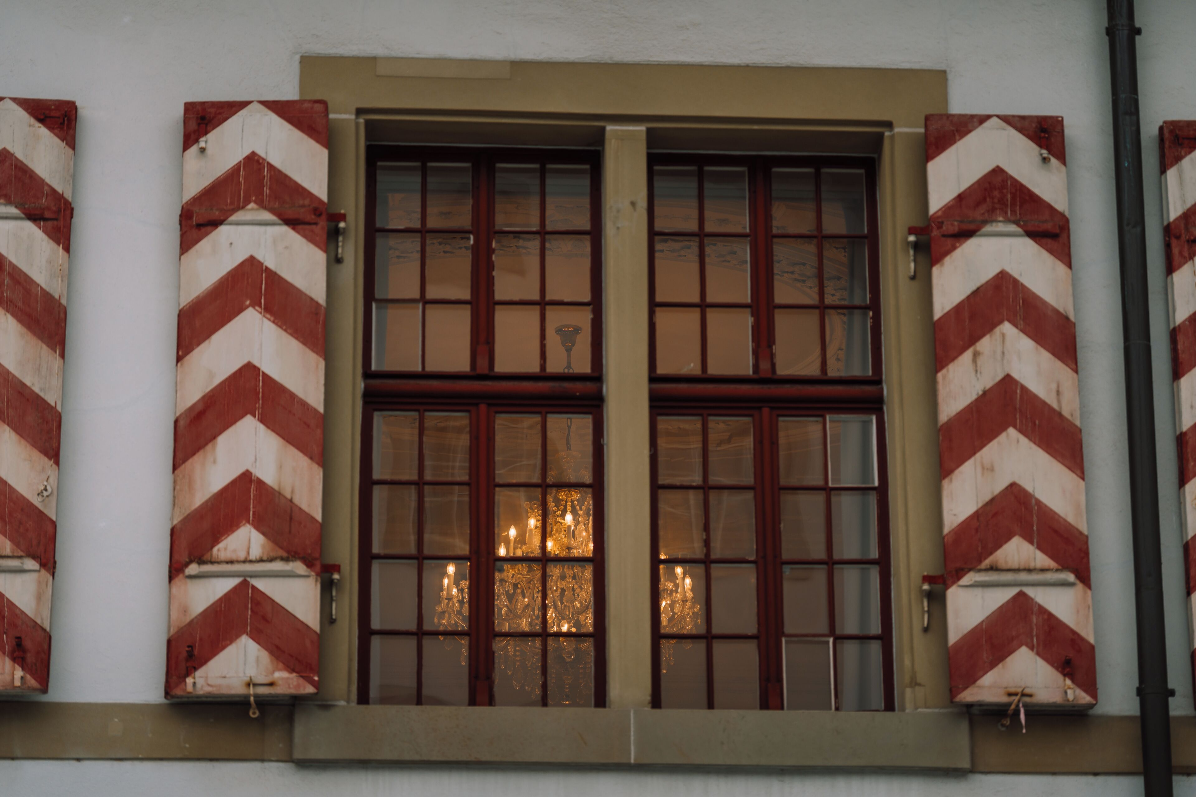 Una ventana de dos cristales, con contraventanas de diseño en forma de flecha, y una luminaria interior visible.