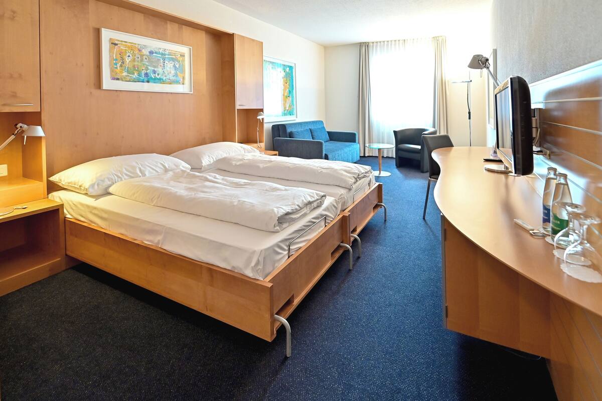 A hotel room with two beds, a desk, a chair, a TV, and artwork on the walls.