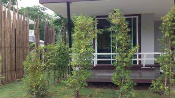 A modern house with a covered porch, surrounded by young trees and a bamboo fence.