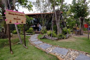 Un letrero de madera anuncia Singha Coffee & House, un jardín con un camino de piedra y mesas al aire libre.