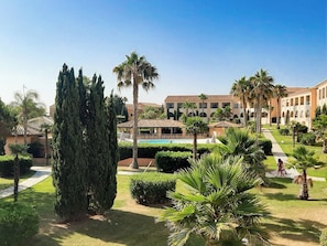 A courtyard with a pool, palm trees, and a building with arched windows. - Résidence Vacancéole Sognu di Mare (Linguizzetta)