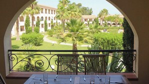 A balcony with a view of a courtyard with palm trees and a building with arches.