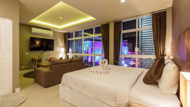 A hotel room with a large bed, a sofa, a TV, and a view of the city at night.