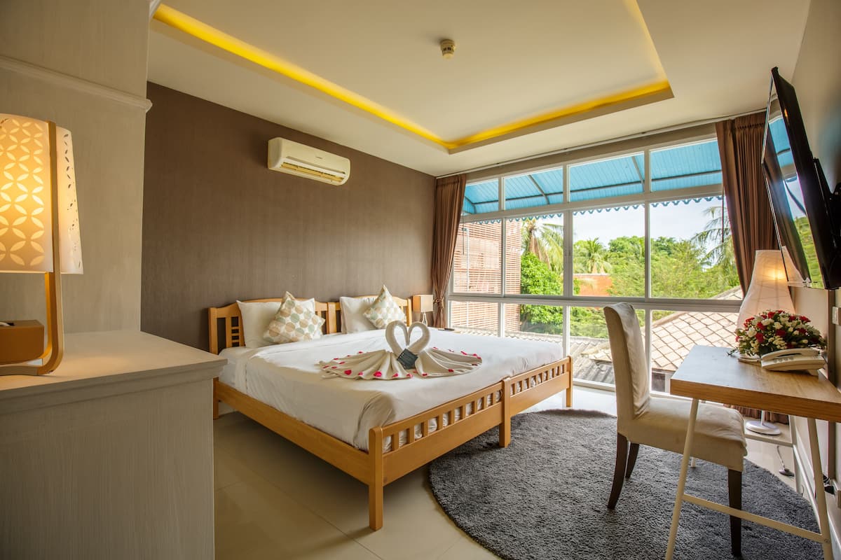 Habitación de hotel con cama, escritorio, silla, televisor y ventana con vistas a zonas verdes.
