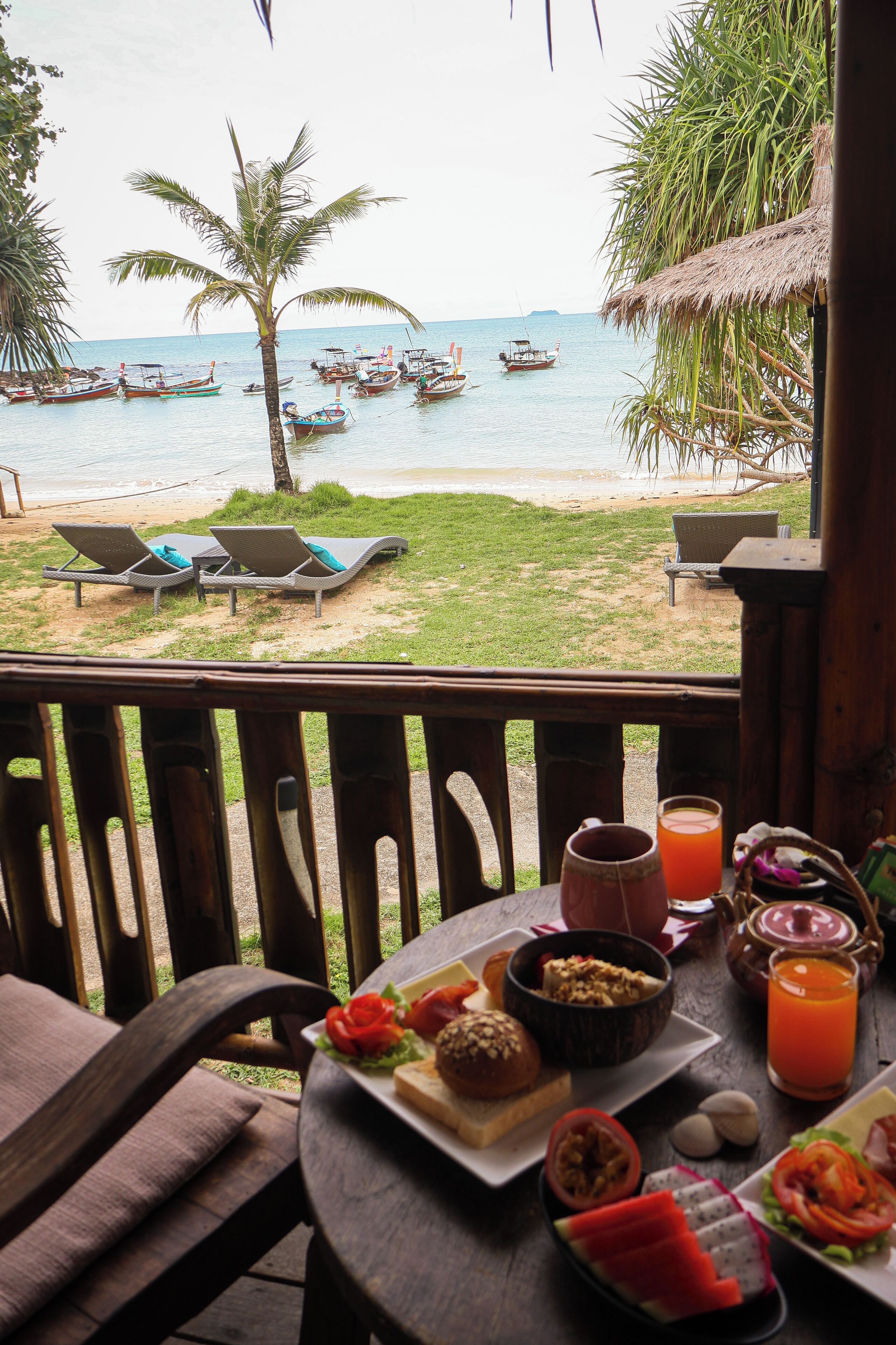 Una mesa con alimentos para el desayuno y vistas a la playa con barcos.