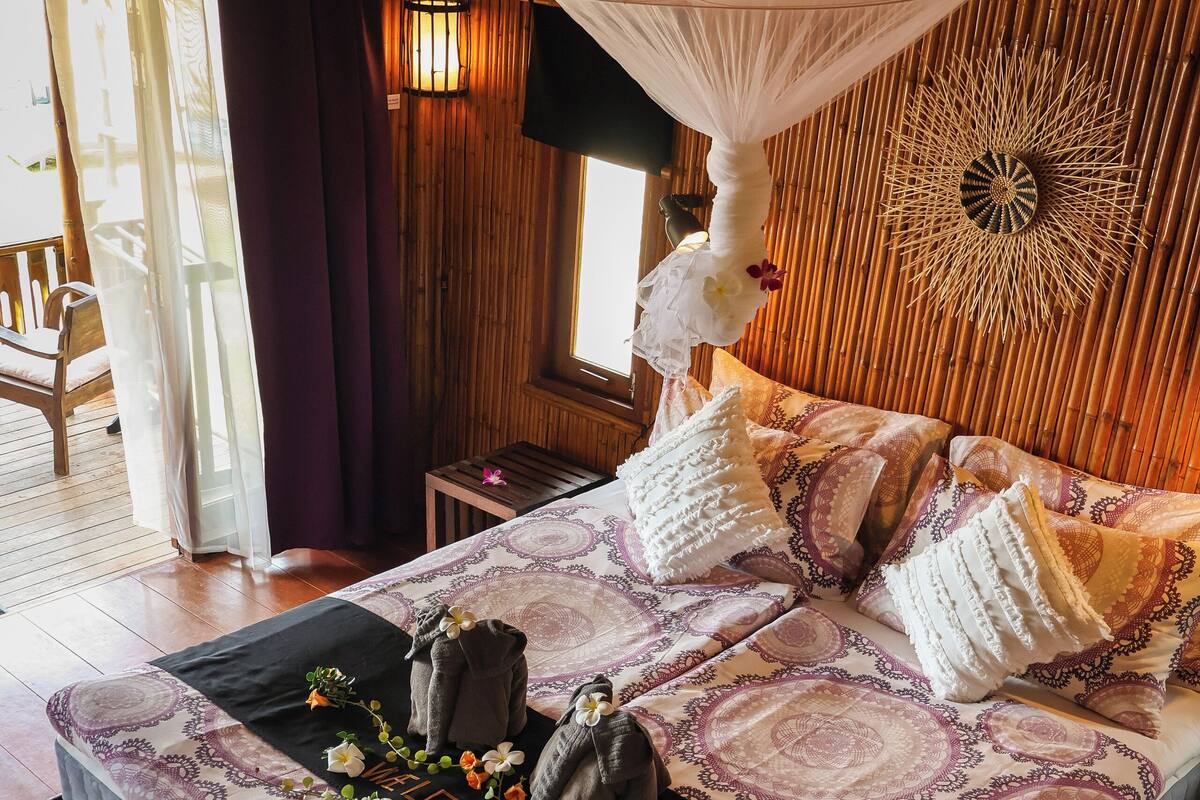 A bedroom with a bed, a hanging mosquito net, a decorative wall, and a wooden floor.
