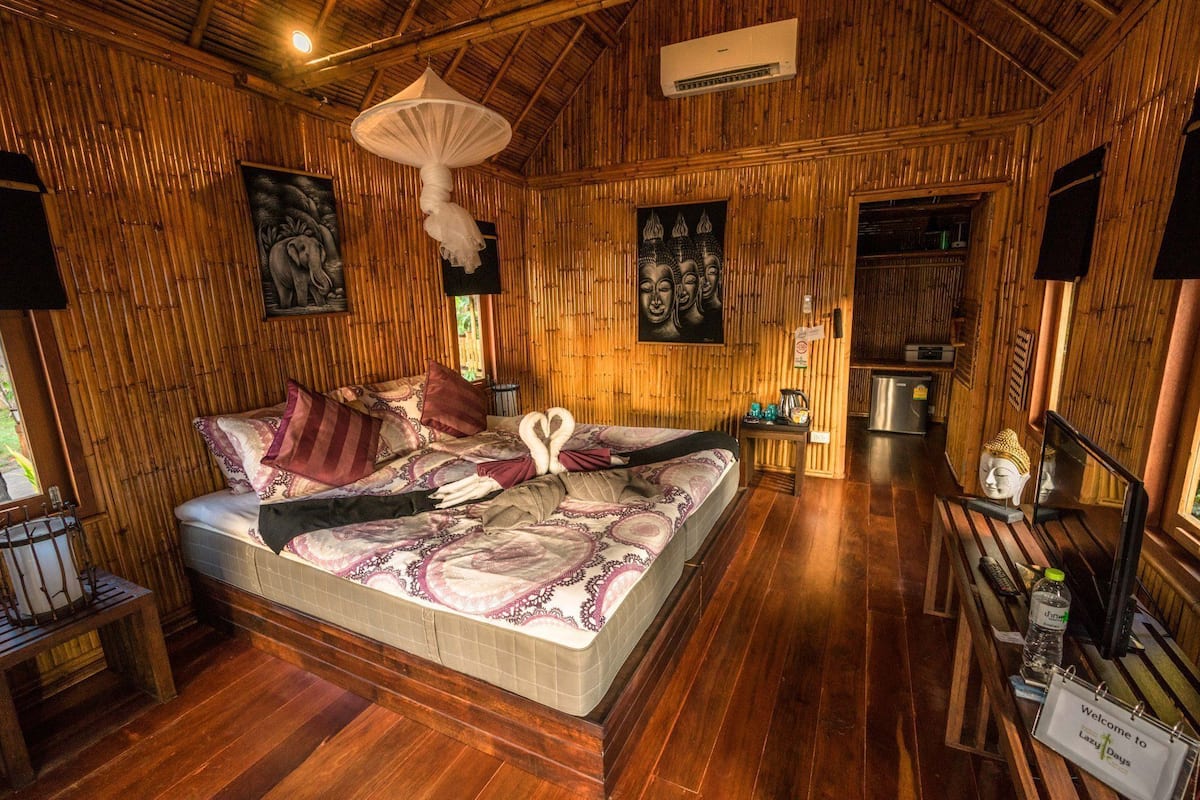 A wooden room with a bed, a hanging light fixture, and a small table with a bottle and a sign.