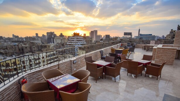 Une terrasse sur le toit, aménagée avec des meubles en osier, offrant une vue sur la ville au coucher du soleil.