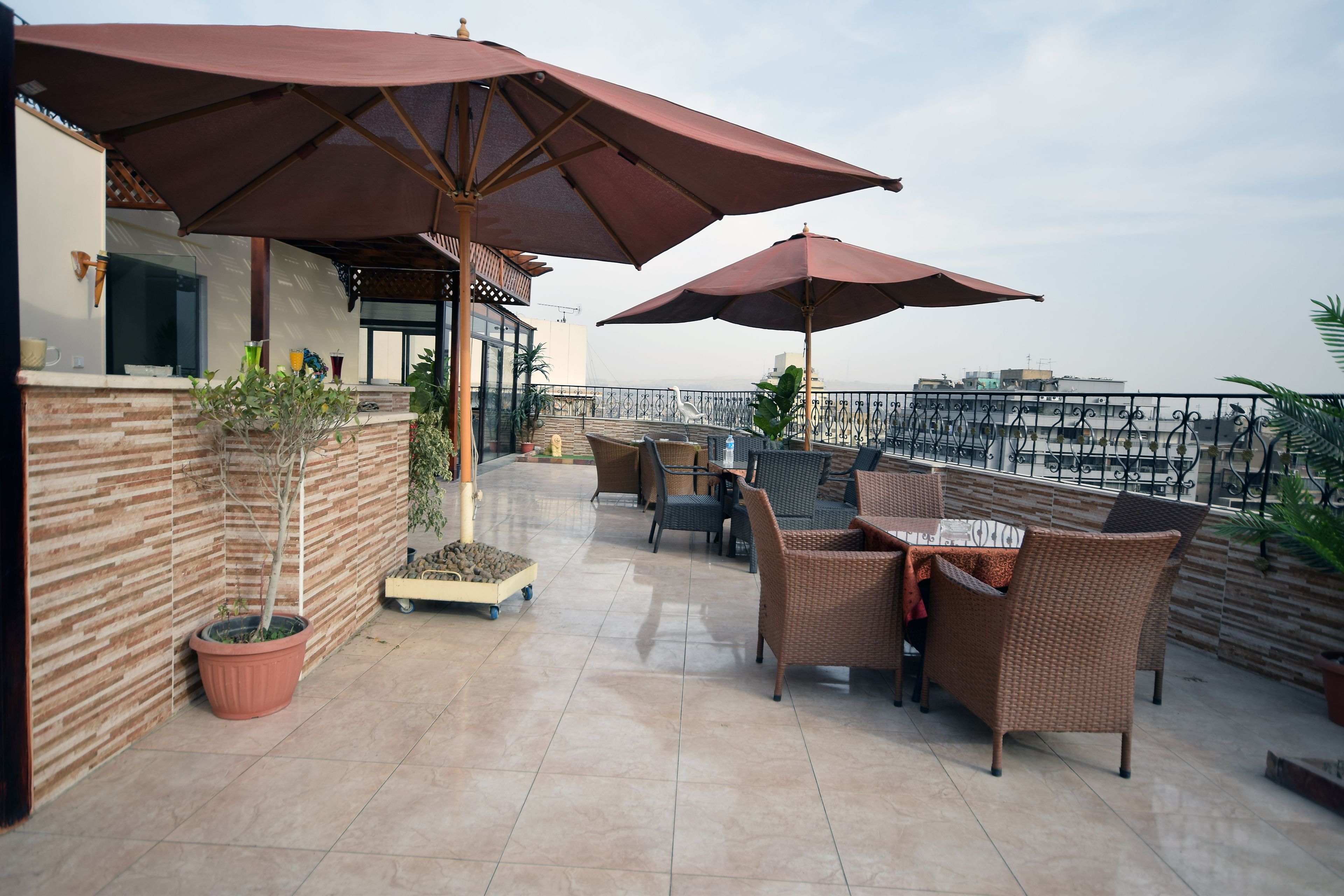 Terraço no telhado com móveis de vime, plantas em vasos e grandes guarda-sóis.