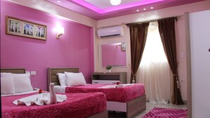 Une chambre d’hôtel avec deux lits, des murs roses, un grand miroir, un appareil de climatisation et une fenêtre avec des rideaux.