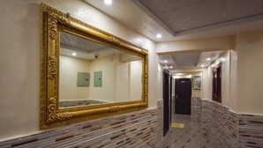 Un couloir orné d’un grand miroir, dont le sol est recouvert de carreaux aux motifs décoratifs, et une porte se trouve au fond.