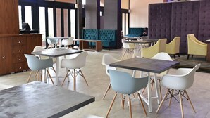 A modern dining area with multiple tables and chairs, a wooden cabinet, and a large cushioned seating area. - Regal Inn Gateway Umhlanga (Umhlanga)