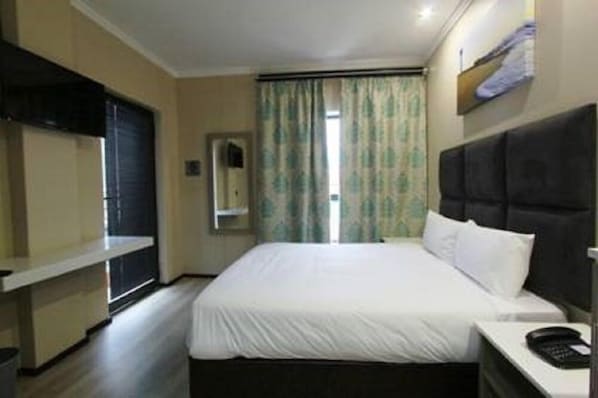Una habitación de hotel con cama, mesita de noche, televisor montado en la pared y ventana con cortinas.