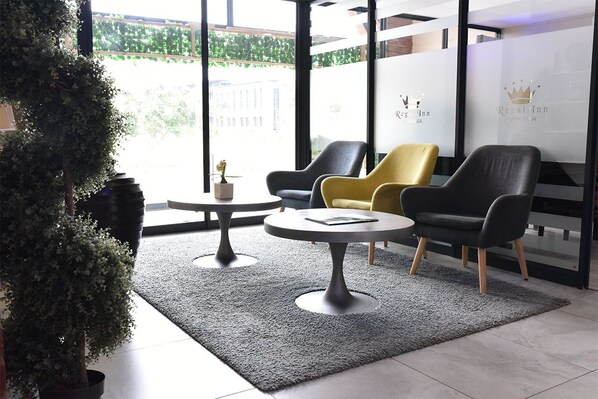 A modern lobby with a reception desk, two round tables, and three chairs. - Regal Inn Gateway Umhlanga (Umhlanga)
