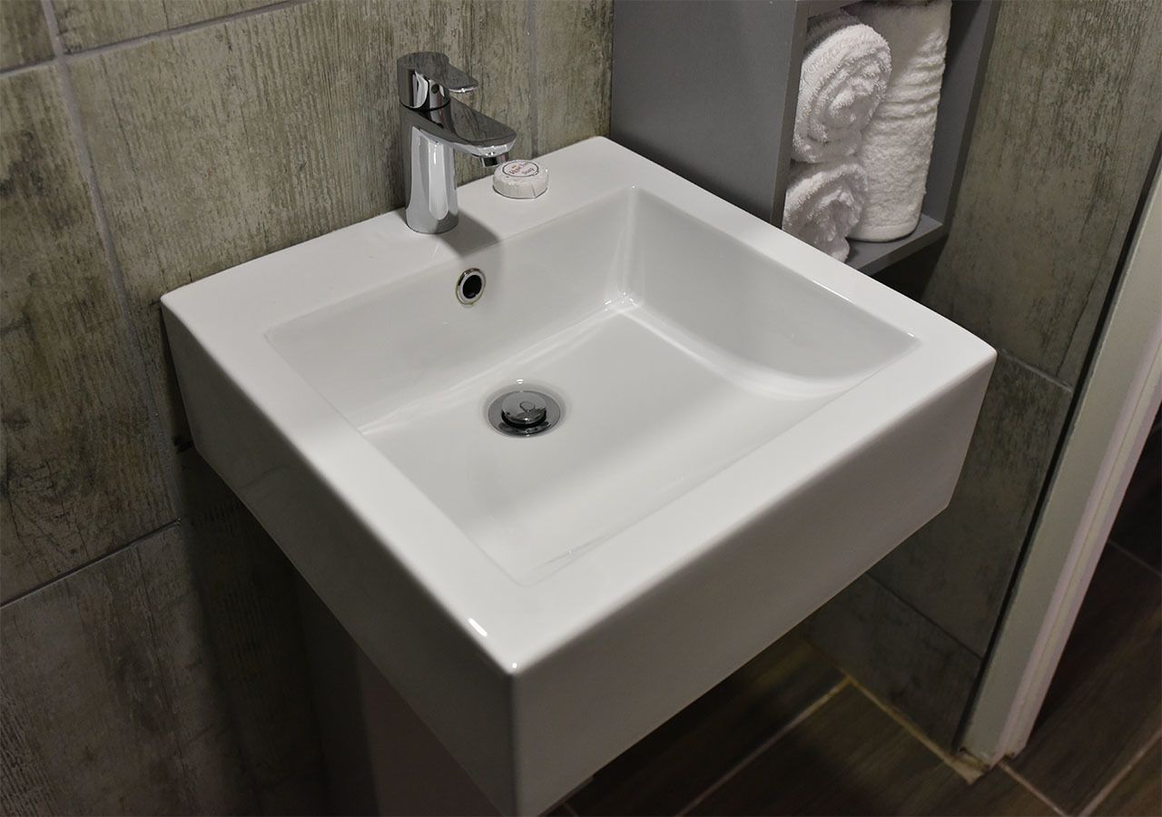 Un lavabo blanc pour la salle de bain, doté d’un robinet chromé et d’un distributeur de savon.