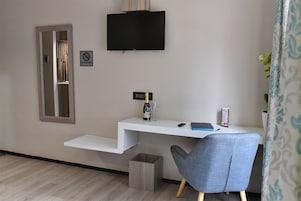 Una habitación moderna con un escritorio blanco, un televisor montado, una silla y un pequeño cubo de basura.