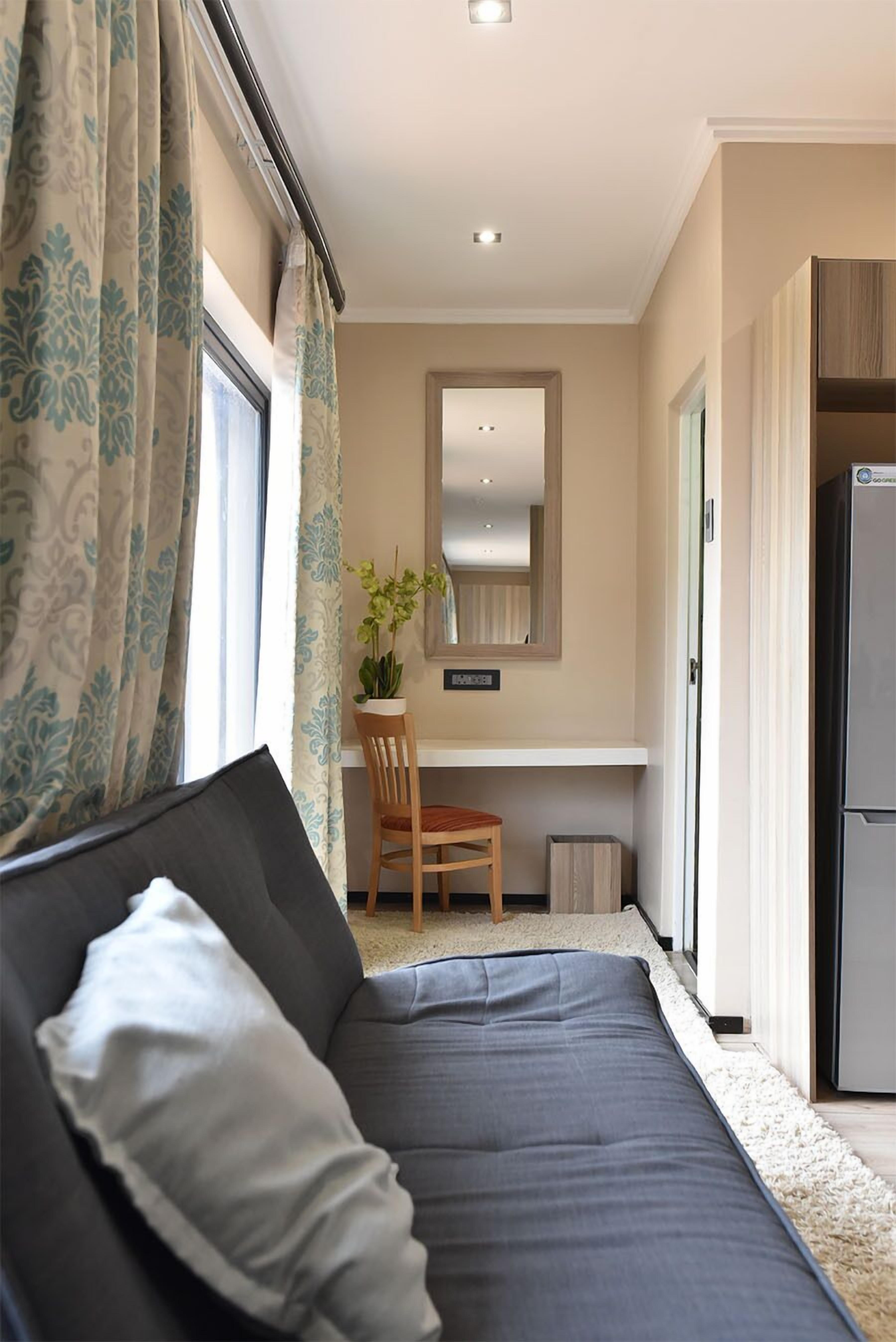 Ein Zimmer mit Bett, Schreibtisch, Stuhl, Topfpflanze und Kühlschrank.