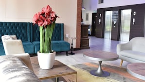 A modern lobby with a teal sofa, a white armchair, a round table, and a potted plant with red flowers. - Regal Inn Gateway Umhlanga (Umhlanga)