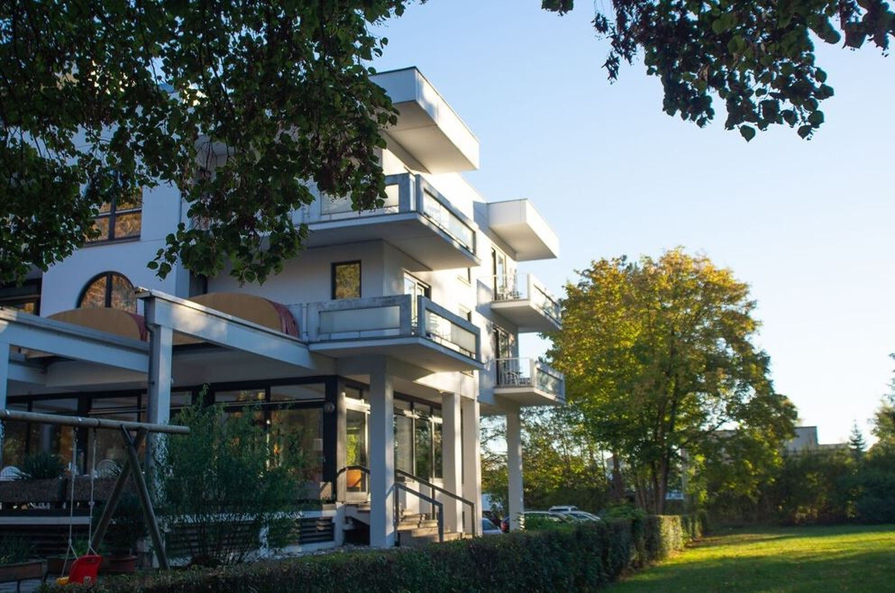 Un edificio moderno de varios pisos con balcones, un espacio al aire libre cubierto y un jardín bien cuidado.
