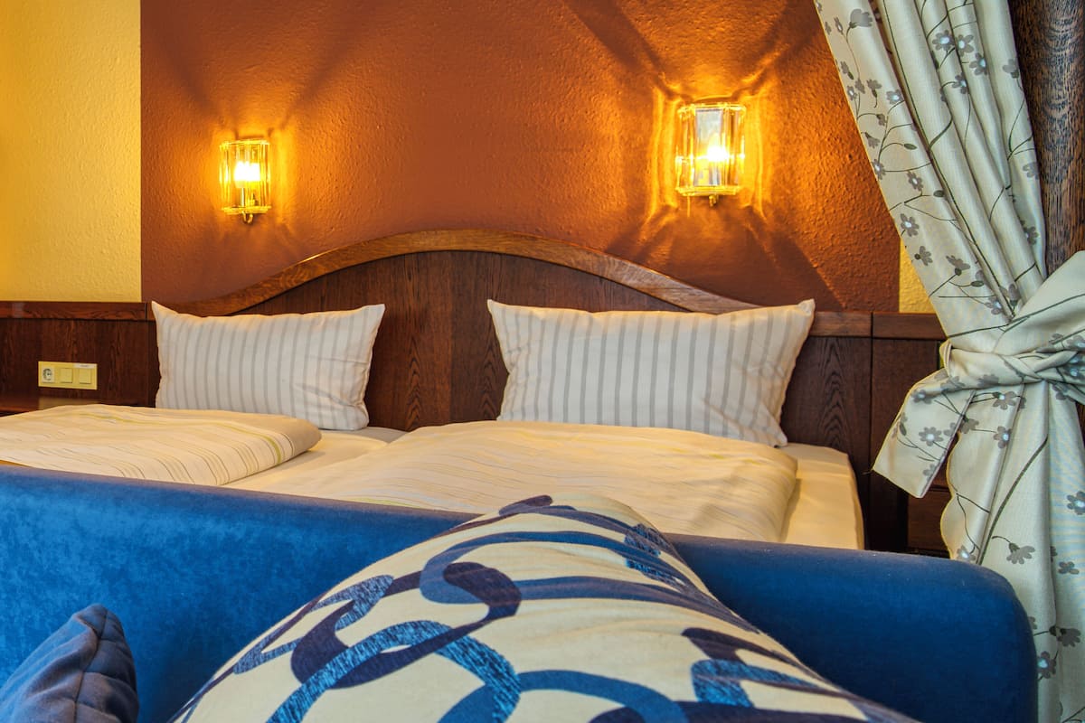 Quarto de hotel com cabeceira de madeira, duas luminárias de apoio e cortina florida.