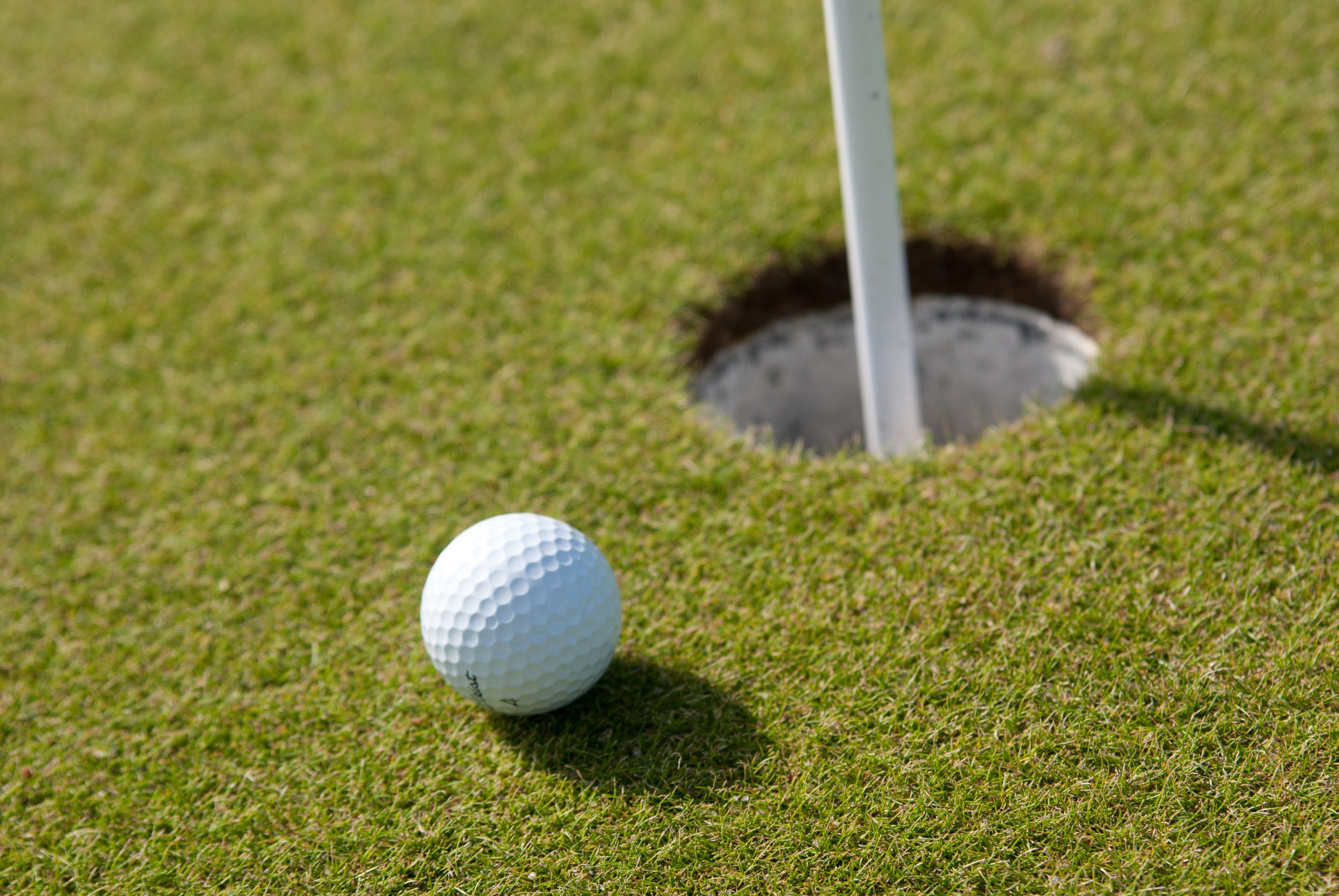 Ein Golfball auf einer Grünfläche, im Hintergrund ein Loch.