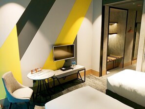 Una habitación de hotel moderna con una televisión de pantalla plana, una mesita redonda pequeña, un sofá y una cama.