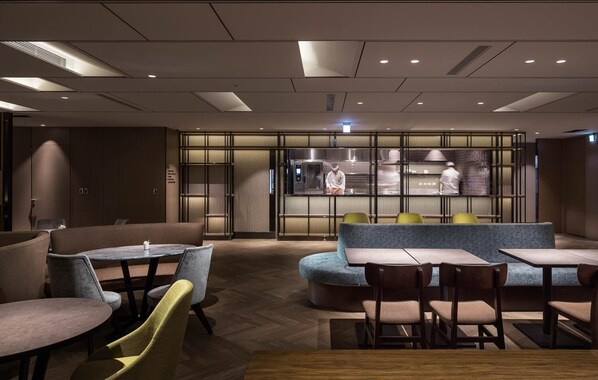 Un restaurante moderno con cocina central, zonas de estar con mesas y sillas, y suelo de madera.