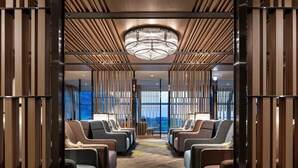 A modern hotel lobby with a row of leather armchairs, a chandelier, and a view of the city through large windows. - Plaza Premium Lounge Terminal 2 Zone A (Taoyuan City)