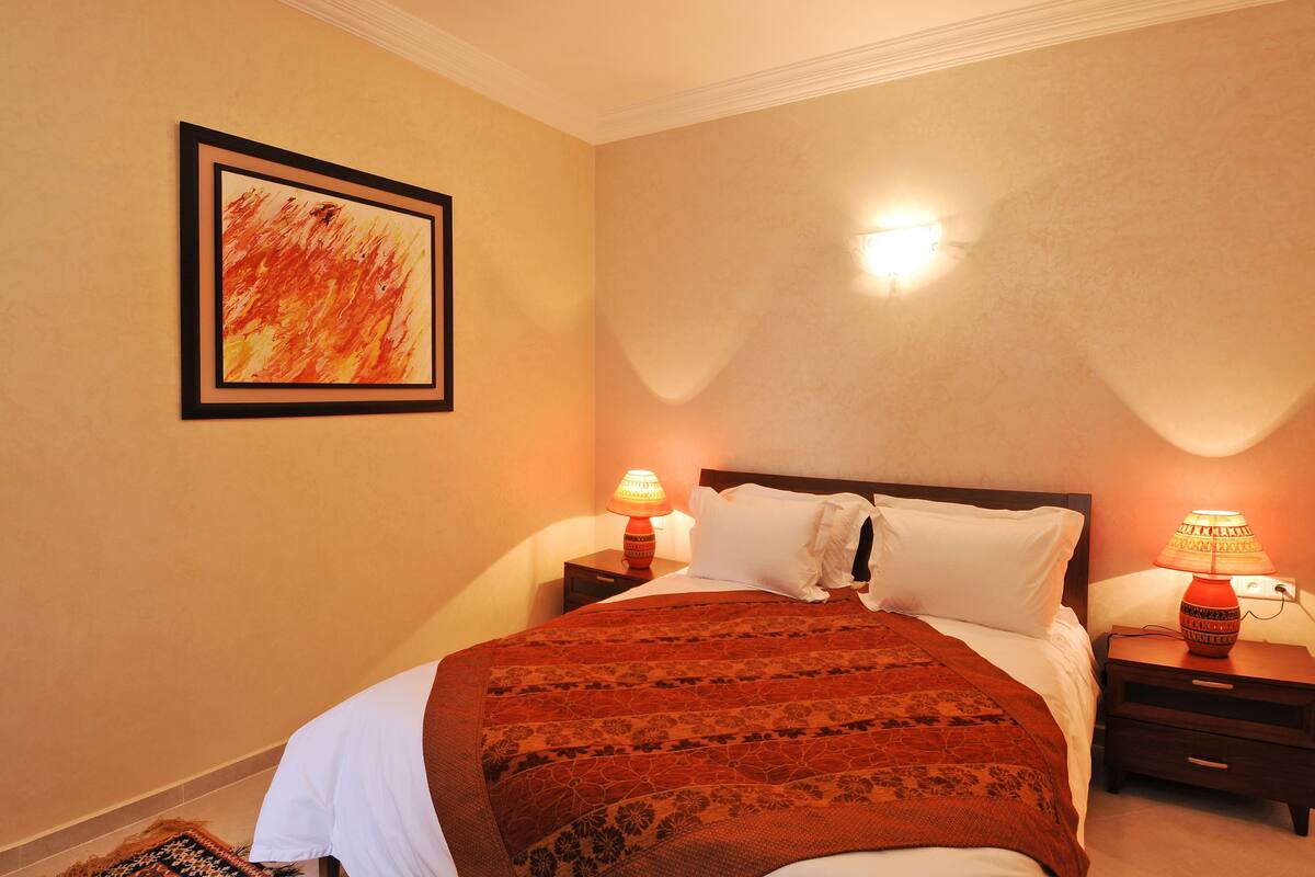 Una habitación de hotel con una cama, dos mesitas de noche, una lámpara de pared y un cuadro enmarcado.