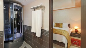 Un baño moderno con ducha acristalada, un perchero para toallas y una cama con mesita de noche y lámpara.