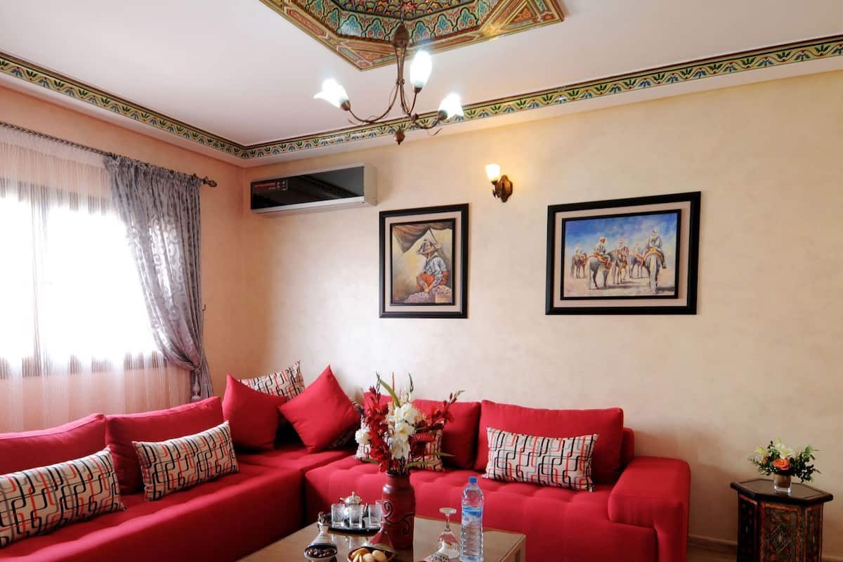 Un sofá rojo con cojines estampados, una mesa de centro con adornos, y dos cuadros enmarcados en la pared.