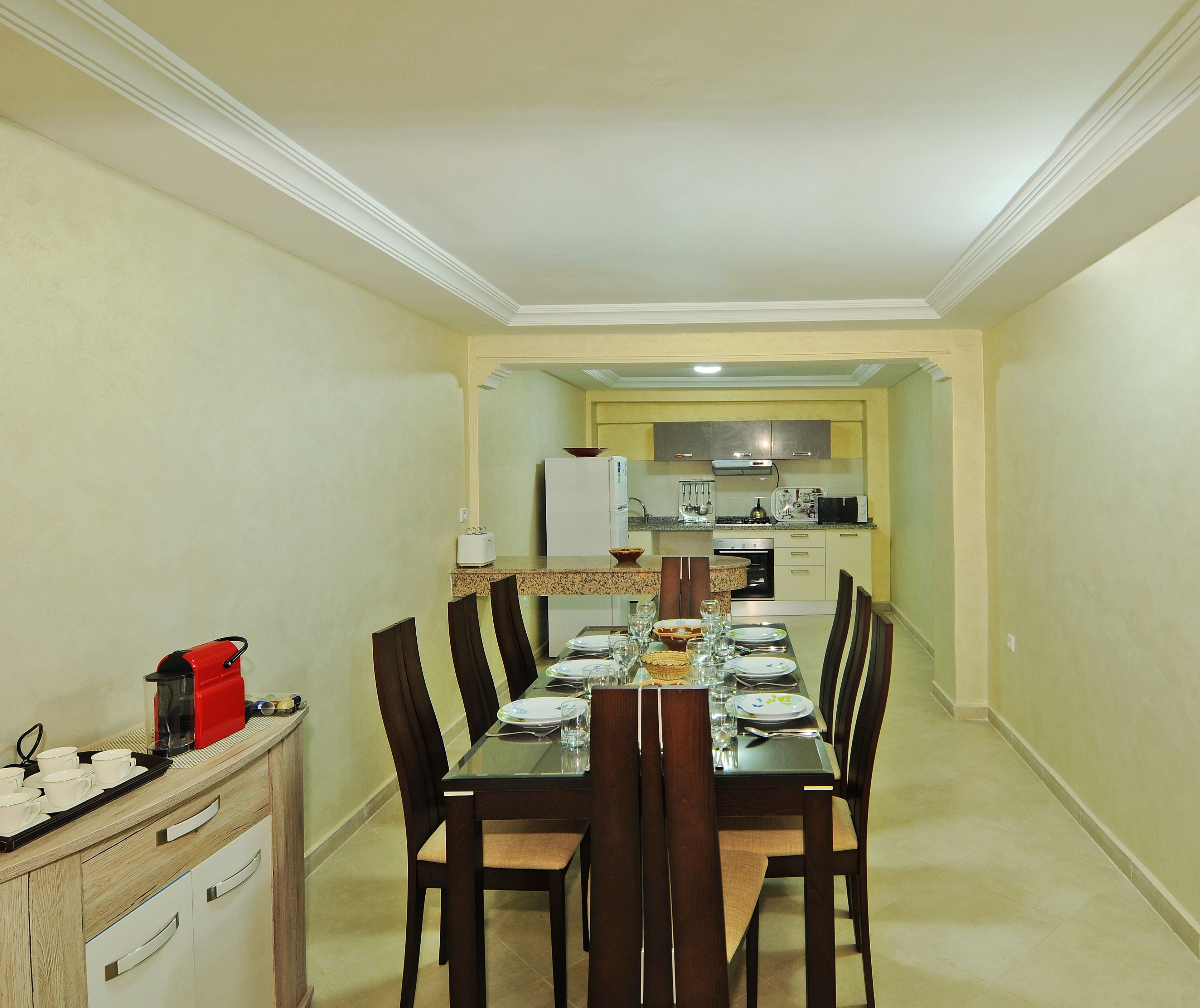 A dining area with a table set for four, a kitchen in the background, and a small kitchenette to the left.