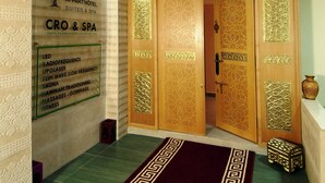 Entrada de hotel con mostrador de recepción, un letrero en la pared que enumera servicios como iluminación LED, radiofrecuencia y masajes, y una puerta de madera tradicional con tallas intrincadas.