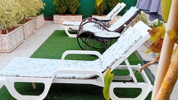 A patio area with two white sun loungers, a small round table, and potted plants.