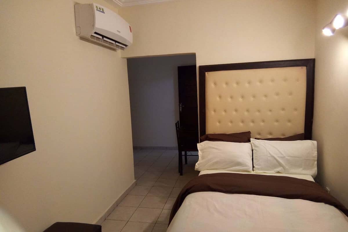 A hotel room with a bed, a flat-screen TV, an air conditioning unit, and a door leading to another room.