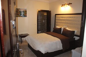 A bedroom with a large bed, a bedside table, a small table, and a painting on the wall. - Hotel Saphir (Abidjan)