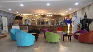 A lobby with a stone wall, a bar area, and colorful chairs. - Hotel Saphir (Abidjan)