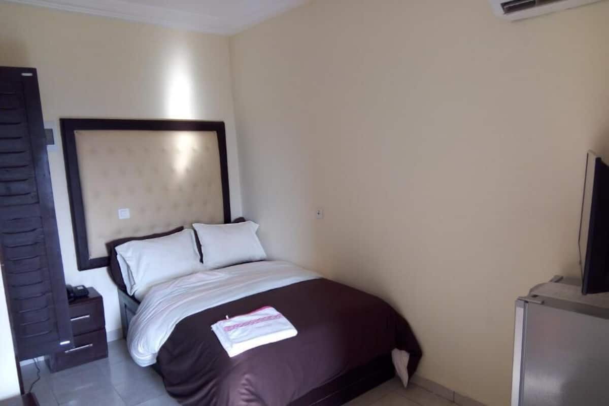 A hotel room with a bed, a desk, a chair, a TV, and a wardrobe.