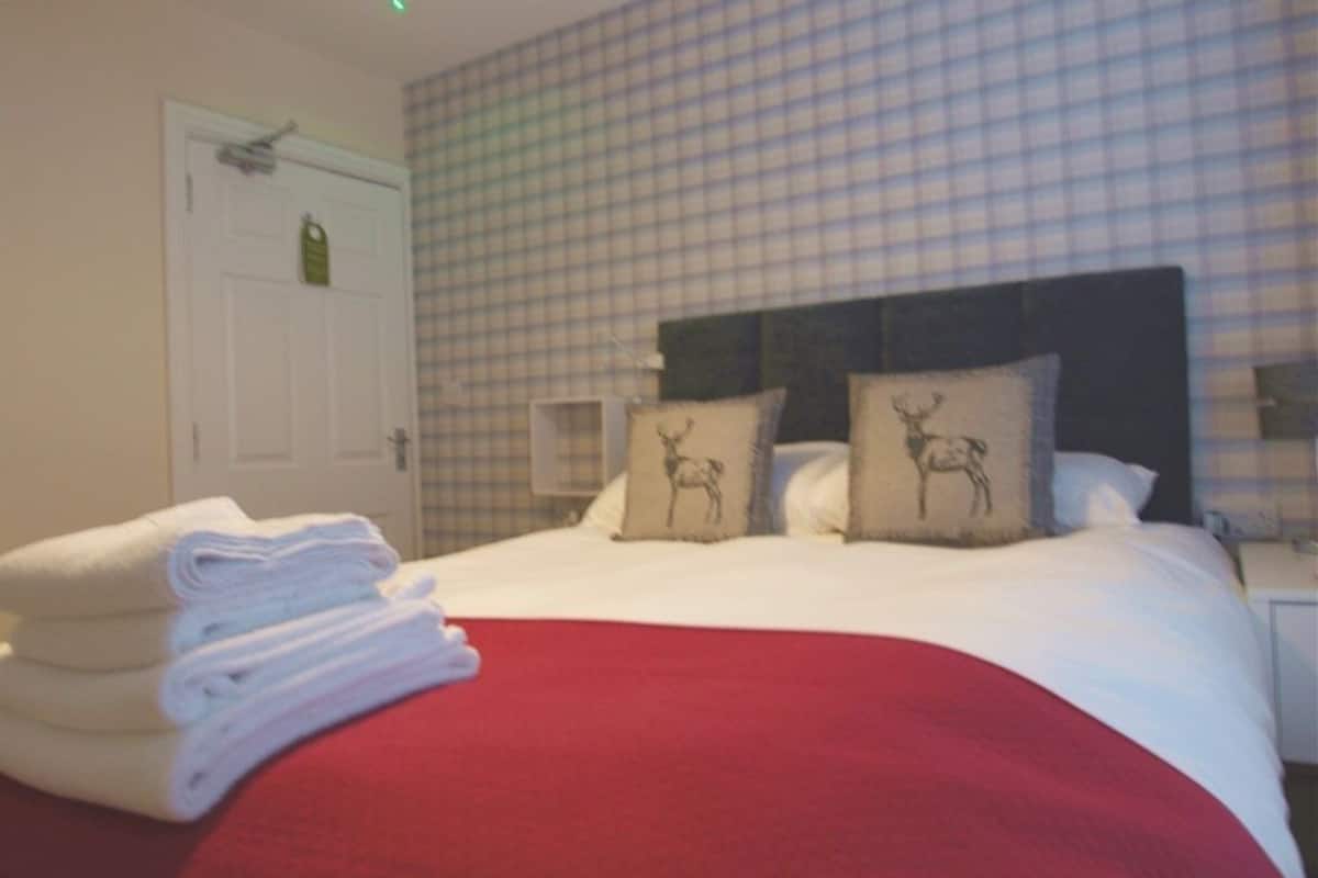 A hotel room with a checkered wall, a bed with white bedding and two pillows with deer designs, and a stack of white towels on the bed.