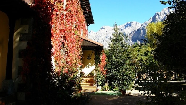 A mountain lodge with a wooden exterior, a covered porch, and a view of snow-capped mountains. - Hotel Rural Picos de Europa (Posada de Valdeon)