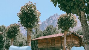A rustic wooden cabin with a red-tiled roof, surrounded by trees and a mountainous backdrop. - Hotel Rural Picos de Europa (Posada de Valdeon)